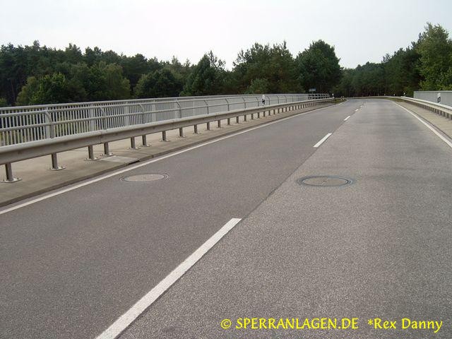 2 Zugänge zu einer unter einer Brücke befestigten Galerie über zwei verriegelte Straßensprengschachtdeckel